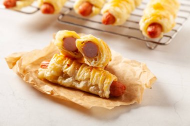 Puf böreğinde pişmiş sosis. Susam tohumları serpilmiş, sosla servis edilmiş. Taş arkaplan.