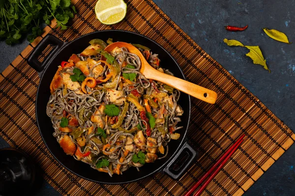 Wheat noodles with black sesame, fried in a wok with chicken and vegetables. Top view.