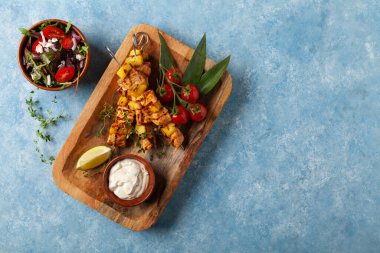Somon ve ananaslı ızgara şiş kebap. Yoğurt sosuyla servis edilir. Mavi boyalı arkaplan.