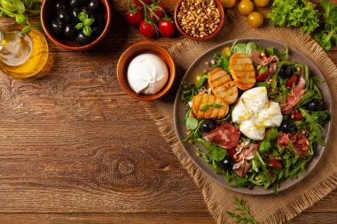 Salad with burrata cheese and croutons. Wooden background.