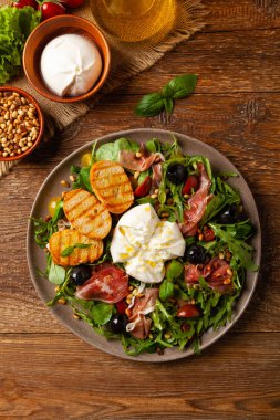 Salad with burrata cheese and croutons. Wooden background.
