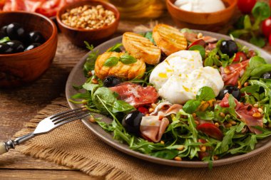 Salad with burrata cheese and croutons. Wooden background.