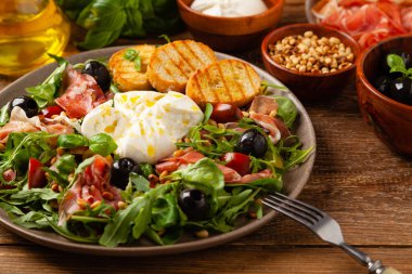 Salad with burrata cheese and croutons. Wooden background.