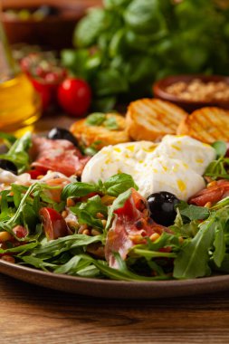 Salad with burrata cheese and croutons. Wooden background.