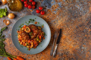 Ossobuco haşlanmış sebzelerle servis edilir. Renkli bir geçmiş. Gri tabak.