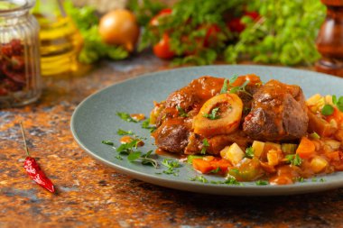 Ossobuco haşlanmış sebzelerle servis edilir. Renkli bir geçmiş. Gri tabak.