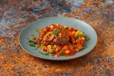 Ossobuco haşlanmış sebzelerle servis edilir. Renkli bir geçmiş. Gri tabak.