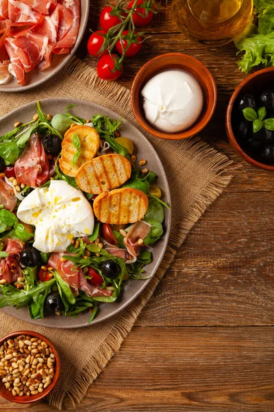 Salad with burrata cheese and croutons. Wooden background.