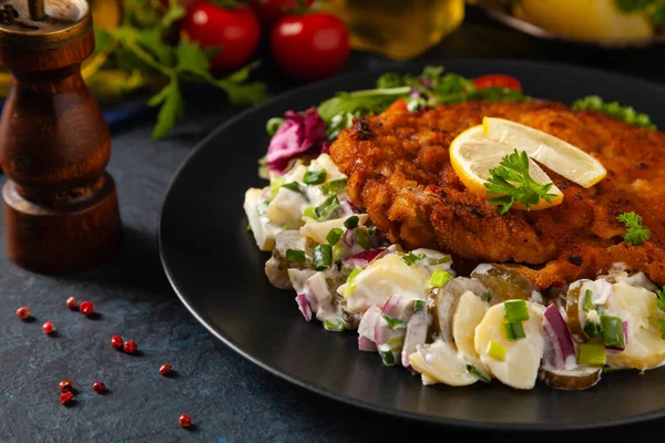 Klasik, geleneksel Viyana sığır filetosu şnitzel. Patates salatasında servis edildi. Üremiş. Koyu arkaplan.