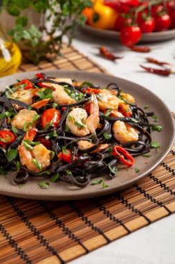 Kızarmış karidesli siyah makarna. Tabakta servis edilmiş. Taş zemin. Yemek çubuğu ya da çatal.