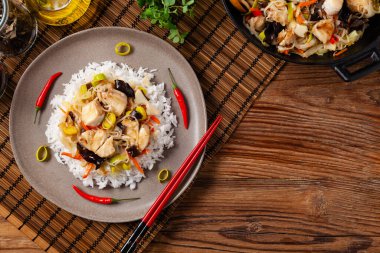 Çin usulü morina balığı, beyaz pirinçli bir tabakta servis edilir. Doğal ahşap zemin. 