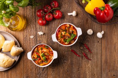 Chicken stew with peppers, mushrooms and tomatoes. Wooden background. 