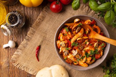 Chicken stew with peppers, mushrooms and tomatoes. Wooden background. 