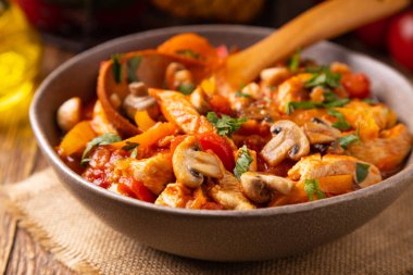 Chicken stew with peppers, mushrooms and tomatoes. Wooden background. 