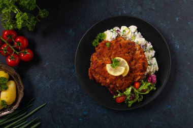 Klasik, geleneksel Viyana sığır filetosu şnitzel. Patates salatasında servis edildi. Üremiş. Koyu arkaplan.