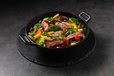 Beef with vegetables. Prepared in a wok. Dark background.