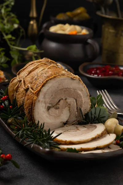 Whole cooked bacon roulade. Tied with a string. Served with cranberries, mushrooms or pickled cucumbers. Dark background.