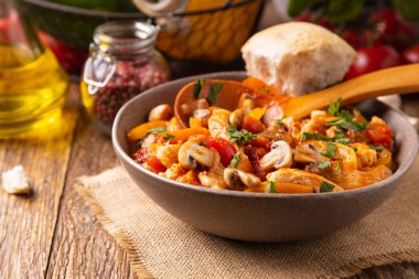 Chicken stew with peppers, mushrooms and tomatoes. Wooden background. 
