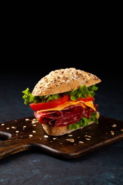 Çoklu tahıllı rulo içinde salamlı ve peynirli sandviç. Kötü ruh hali. Siyah arkaplan.