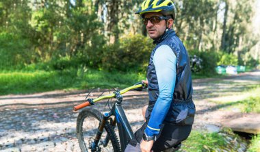 Bisikletinin üzerinde oturan dağ bisikletçisinin portresi. Kaskı, gözlükleri ve akıllı gözlüğü vardı.