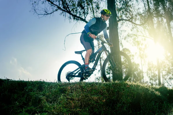 骑自行车的男骑手骑自行车在山边的森林里 身后有太阳 — 图库照片