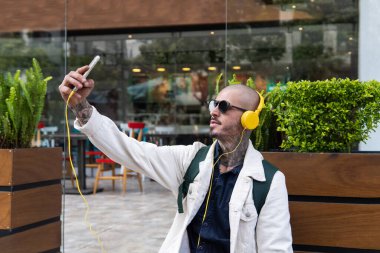 Kulaklıklarıyla müzik dinleyen ve kaldırımda selfie çeken bir adam.