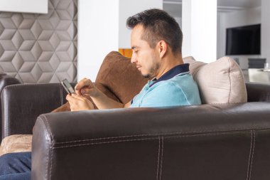 Adam evinin oturma odasında cep telefonuyla iş yapıyor. Ev kavramından çalış