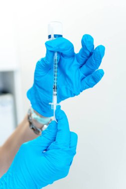 Close-up of the hands of a doctor or nurse with blue surgical gloves preparing a syringe with medicine from a container