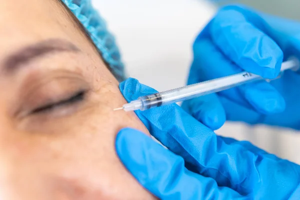 Close-up of the hands of a doctor who injects hyaluronic acid to a patient next to her eye. Health and rejuvenation concept