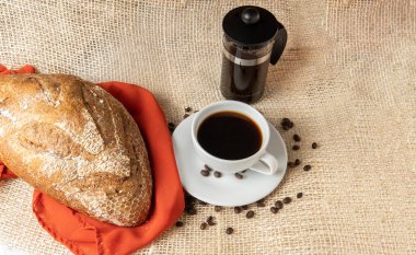 top view of a cup of coffee a french press and a loaf pan on a jute background. Breakfast concept with copy space