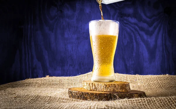 Beer can serving in a crystal glass on a blue wooden textured background