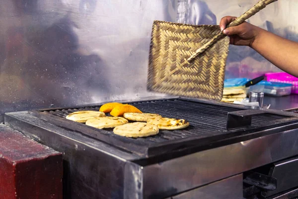 Close-up of a woman\'s hand fanning the charcoal from the grill to prepare Colombian empanadas and arepas with a fan