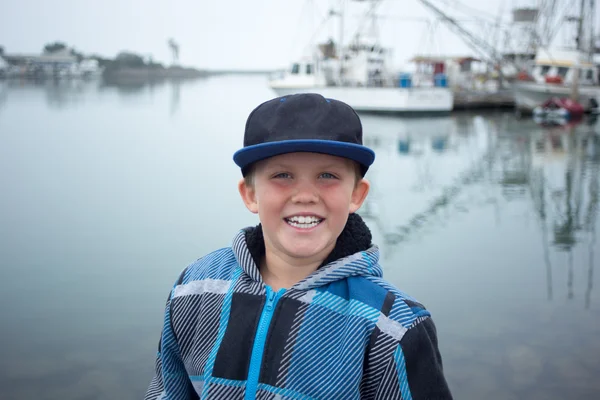 Un garçon heureux assis au bord du port Photos De Stock Libres De Droits