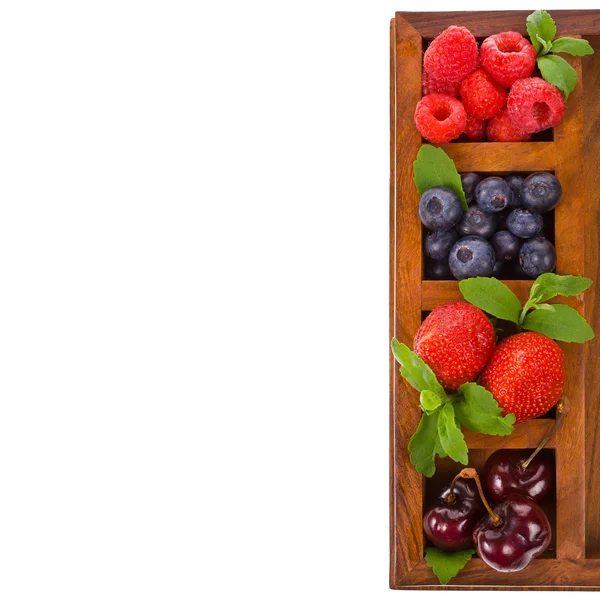 Mirtilos, morango, framboesas e cereja em uma bandeja de madeira isolada em fundo branco — Fotografia de Stock