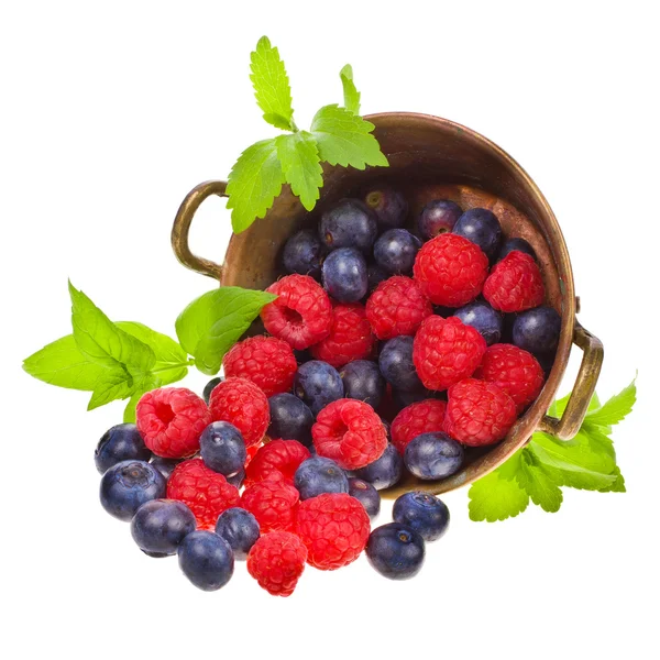 Raspberries and blueberries scattered from the old copper basin isolated on white background — Stock Photo, Image