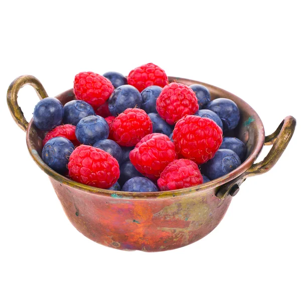 Raspberries and blueberries scattered from the old copper basin isolated on white background — Stock Photo, Image