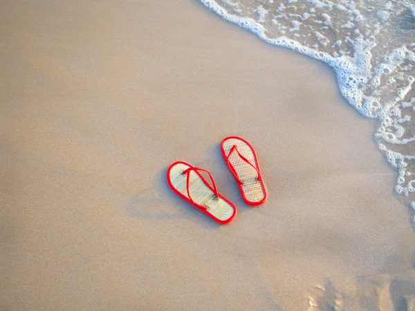 休日のテーマ - 赤いスリッパ砂と海の波に横たわっていた — ストック写真