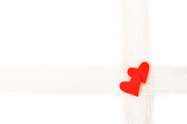 Подарочное оформление - две светлые льняные ленты и фигуры в виде красных сердец, выделенных на белом фоне — стоковое фото