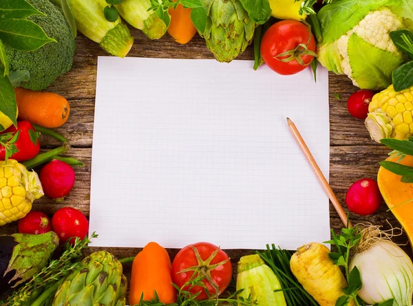 Topic cooking - lots of different vegetables and herbs on an old wooden and paper notebook for recipes board as a background