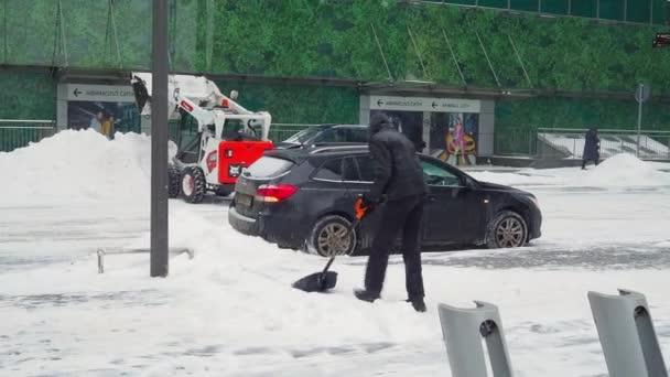 Seorang pekerja utilitas menyekop salju dengan sekop di jalan kota selama salju turun pada hari musim dingin. — Stok Video
