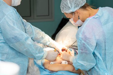 Cerrahi üniformalı bir kadın cerrah ve tıbbi maske bir hastayı ameliyat eder.