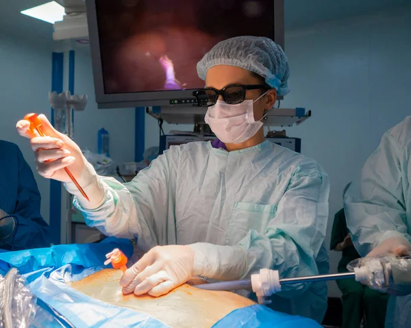 A woman surgeon in 3D glasses inserts an instrument into the patients body