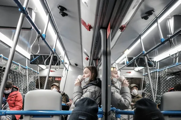 Een jonge vrouw met een beschermend masker op de bus drinkt koffie uit een papieren beker — Stockfoto