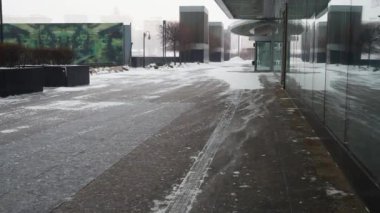 Rüzgâr tarafından taşınan kar, bilinmeyen modern bir binanın yanında cam bir cephede yürür.. 