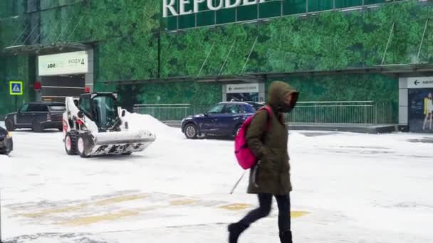 Um pequeno carregador com um balde remove a neve de uma estrada em uma rua da cidade — Vídeo de Stock