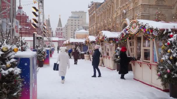 Varios turistas caminan a través de la Feria de Año Nuevo en Red Square en un día de invierno durante una nevada. — Vídeo de stock