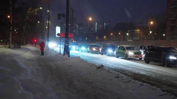 La chica camina por la carretera durante una nevada en los faros de los coches. — Vídeos de Stock