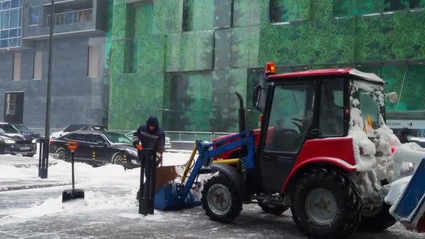 Dělník v zimě odhazuje sníh do kbelíku na traktory. Sníh ve městě. — Stock video