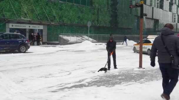 Працівник виносить сніг лопатою на міській вулиці під час снігопаду в зимовий день.. — стокове відео