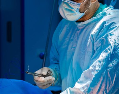 The surgeon holds the surgical needle and suture.